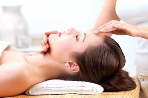 Spa treatment showing facial massage on person's face with white towel headrest