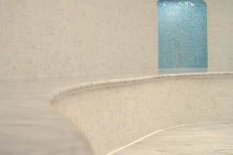 Empty curved indoor pool with cream tile walls and bright turquoise mosaic tile accent panel