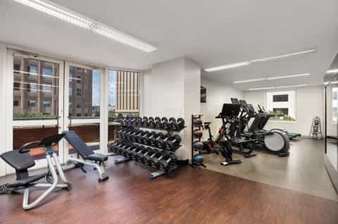 Modern fitness center with dumbbells, stationary bikes, exercise equipment, and city views