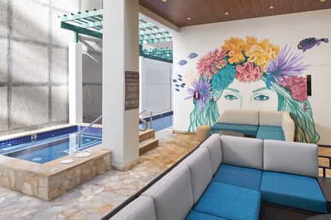 Spa relaxation area with indoor hot tub, colorful floral wall art, and gray modular seating