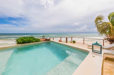 Beachfront infinity pool overlooking turquoise ocean with palm trees and sand