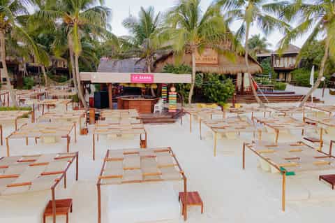 Beach bar scene with colorful stacked lounge chairs, thatched-roof structures, and palm trees