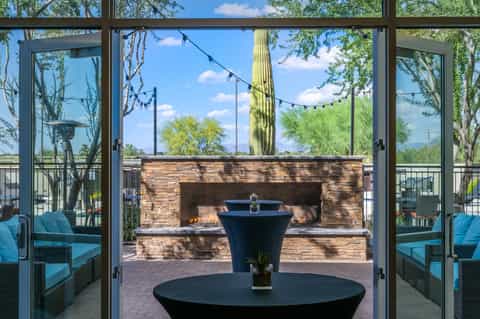 Modern lounge area with large windows overlooking fireplace, patio seating, and desert landscape