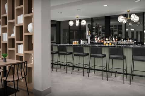 Contemporary hotel bar with black mirror backdrop, pendant lighting, and wooden shelving