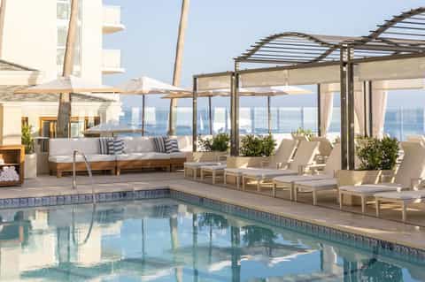 Rooftop pool terrace with ocean view, lounge seating, pergola shade, and white umbrellas