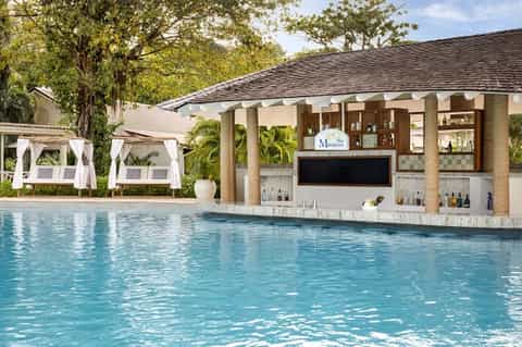 Resort pool bar with white cabanas, tropical landscaping, and covered pavilion