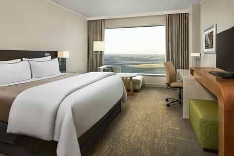 Modern hotel room with city view, queen bed, work desk, and contemporary neutral décor