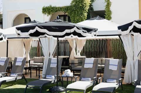 Elegant poolside cabanas with black and white umbrellas, curtains, and lawn seating area