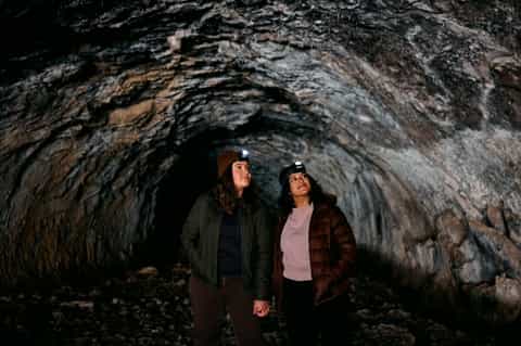 Two visitors exploring an underground cave tunnel with rocky walls and headlamps