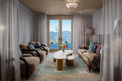 Luxury lounge with mountain and water views through French doors, upholstered seating, and sheer curtains
