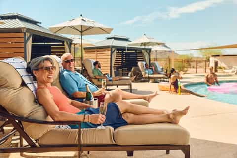 Couple enjoying poolside lounge chairs with umbrellas, cocktails, and desert resort backdrop