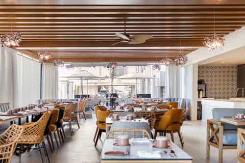 Contemporary restaurant with wooden slat ceiling, crystal chandeliers, yellow chairs, and terrace views