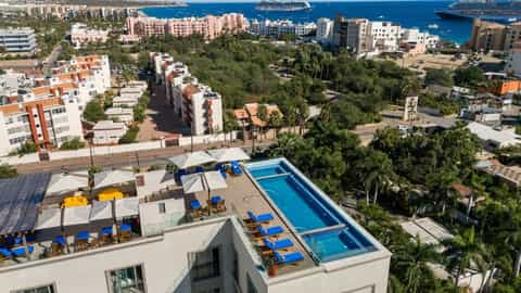 Rooftop pool area overlooking Mediterranean harbor with blue loungers, palm trees, and coastal cityscape