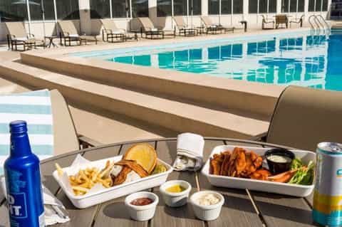 Pool deck with loungers, food and drinks on table, and lap pool in background