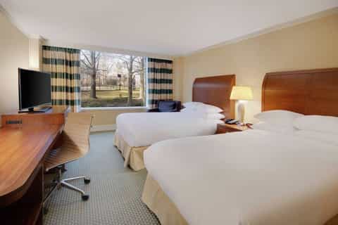 Hotel bedroom with two queen beds, wood headboards, TV, and large window with park views