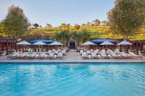 Vineyard pool area with lounge chairs, blue umbrellas, and scenic hillside views