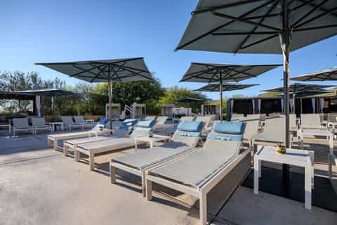 Modern pool area with grey loungers under large cantilever umbrellas on paved deck