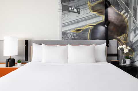 Contemporary hotel bedroom with white bedding, black headboard, urban street art mural, and modern minimalist design