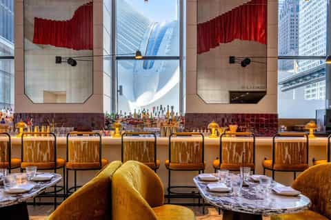 Upscale hotel restaurant bar with marble tables, gold stools, and dramatic red curtain window treatment
