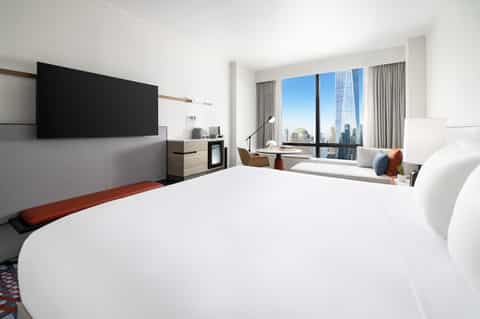 Modern high-rise hotel bedroom with city skyline view through floor-to-ceiling windows and contemporary furnishings