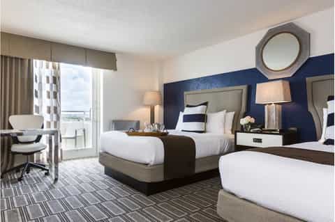 Hotel guest room with navy accent wall, two beds, ocean-view balcony, and modern furnishings