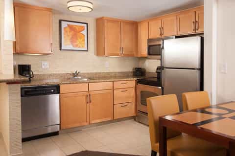 Hotel suite kitchen with wood cabinets, stainless appliances, and dining table