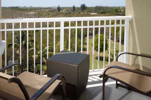 High-rise balcony with white railing, lounge chairs, black side table, and panoramic landscape view