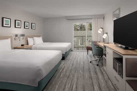 Hotel bedroom with two queen beds, desk area, and glass balcony door