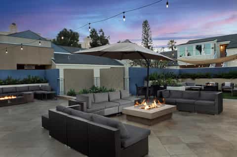 Upscale outdoor lounge at twilight with fire pits, rattan seating, and hanging string lights