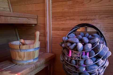 Wooden sauna interior with bucket, ladle, and basket of sauna stones on shelf