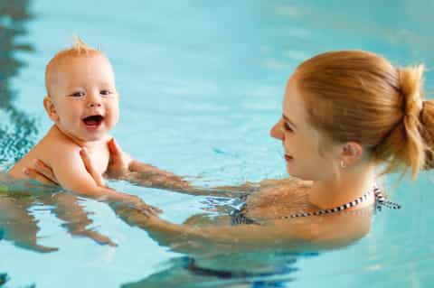 Woman and toddler playing together in a bright blue indoor swimming pool