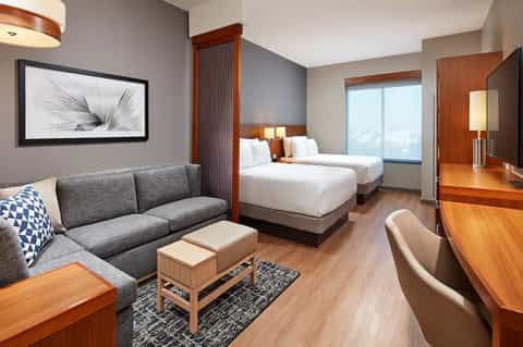 Contemporary hotel room with two queen beds, gray sofa, and wood furnishings