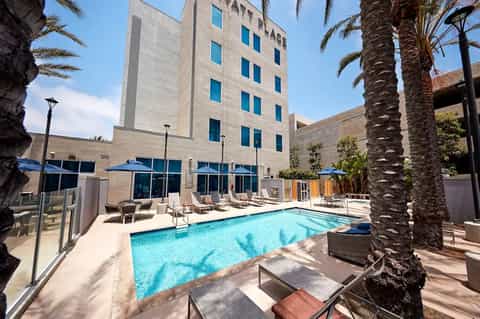 Urban hotel courtyard with heated swimming pool, blue umbrellas, and multi-story building facade