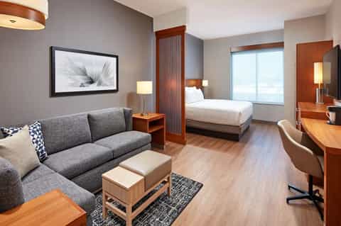 Upscale hotel suite with living area, bed, wood furnishings, and ocean view windows
