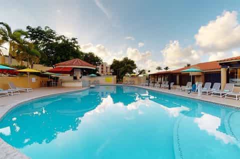 Resort swimming pool with turquoise water, lounge chairs, colorful umbrellas, and tropical landscaping