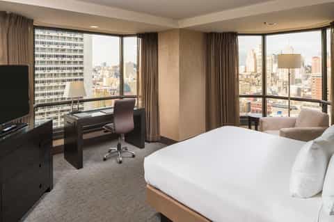 High-rise hotel suite with panoramic city views, work desk, and modern furnishings