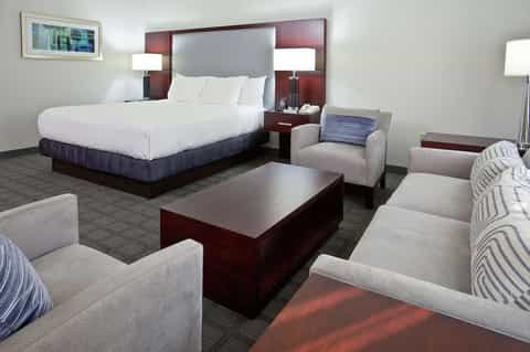 Spacious hotel suite with king bed, sofa, armchairs, and burgundy accents