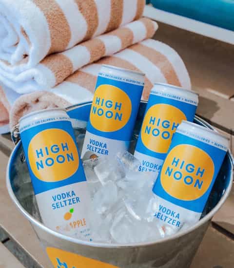 High Noon vodka seltzers in ice bucket with striped towels poolside