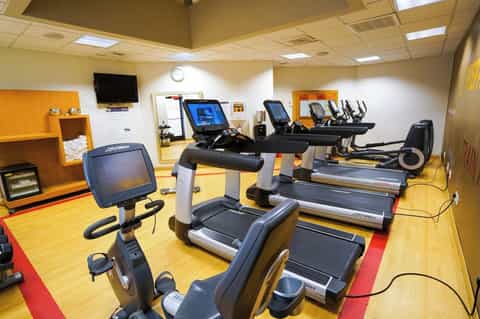 Hotel fitness center with cardio equipment, treadmills, stationary bikes, mirrors, and yellow flooring