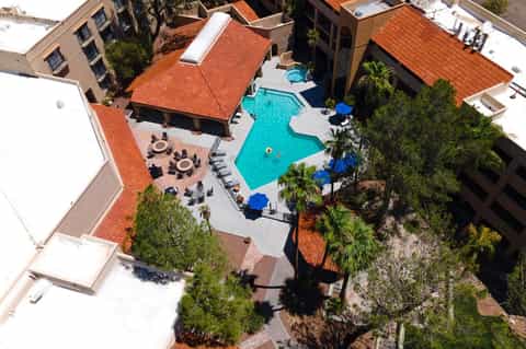 Aerial view of resort pool complex with turquoise water, loungers, fire pits, and surrounding buildings