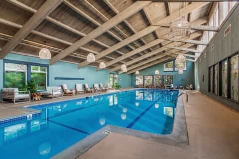 Indoor lap pool with exposed wood beam ceiling, pendant lights, and lounge seating area