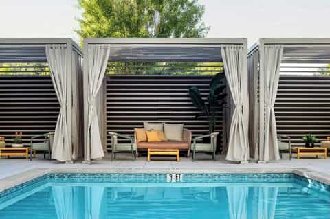 Modern poolside cabana with sheer curtains, lounge seating, and swimming pool reflection