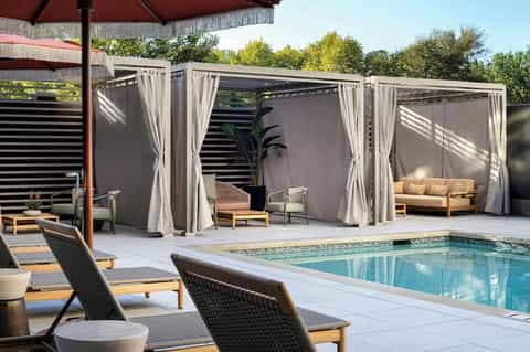 Backyard poolside with modern pergola cabanas, lounge chairs, and stone patio