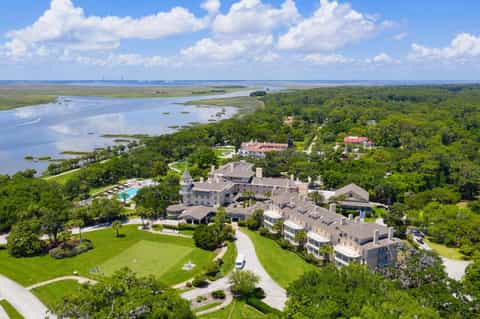 Aerial view of luxury resort with pools, mansion, and grounds overlooking marshlands and river