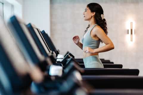 Woman running on treadmill in modern gym with mirrored walls and natural lighting