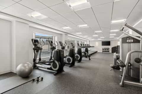 Contemporary fitness center with cardio equipment, dumbbell rack, and access to outdoor patio
