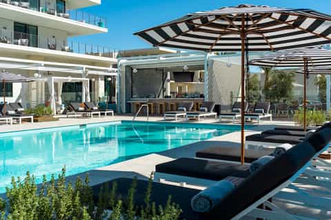 Modern resort pool with striped umbrellas, lounge chairs, and waterfront bar area