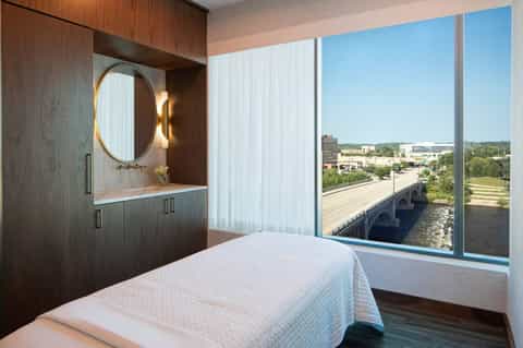 Modern hotel room with river view windows, wooden vanity with circular mirror, and contemporary design