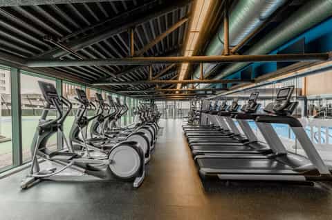 Modern fitness center with rows of treadmills and exercise bikes under industrial ceiling beams
