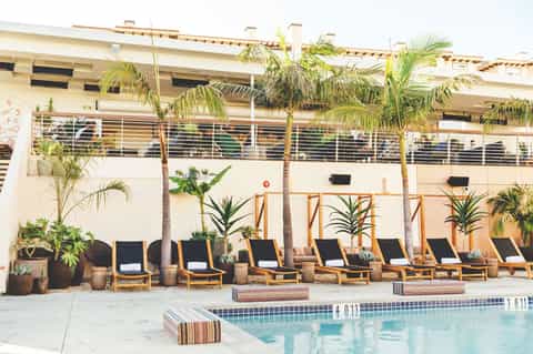 Resort pool area with lounge chairs, palm trees, and multi-story building facade with metal railings